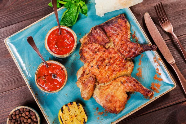 Roasted Chicken or turkey with spices, lemon, tomato sauce, basil and pita bread on plate on dark wooden background. Thanksgiving table served with knife and fork. Top view — Stock Photo, Image
