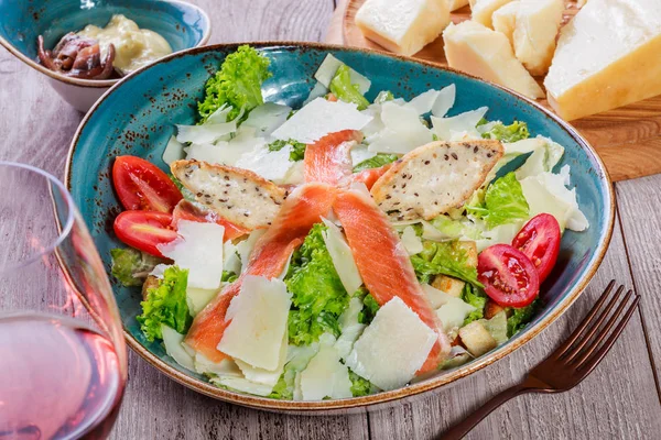 Ensalada de salmón con salsa de atún, queso parmesano, croutons, tomates, verduras mixtas, lechuga y copa de vino sobre fondo de madera. Comida mediterránea. Vista superior — Foto de Stock