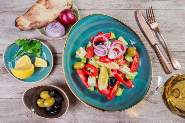 Ensalada griega de verduras ecológicas con tomates, pepinos, cebolla roja, aceitunas, queso feta y copa de vino sobre fondo de madera. Vista superior —  Fotos de Stock