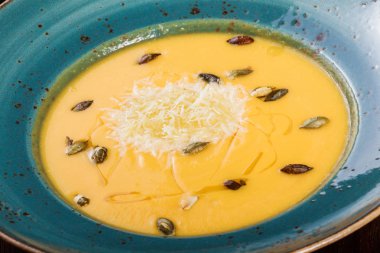 Parmesan peyniri, kabak çekirdeği ve koyu ahşap zemin üzerine ekmek ile kabak ve havuç çorbası