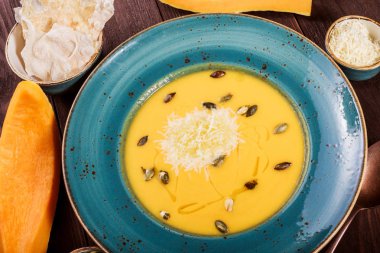 Parmesan peyniri, kabak çekirdeği ve koyu ahşap zemin üzerine ekmek ile kabak ve havuç çorbası. Maddeler tablosundaki. Üstten Görünüm