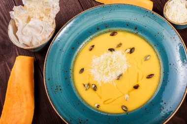 Parmesan peyniri, kabak çekirdeği ve koyu ahşap zemin üzerine ekmek ile kabak ve havuç çorbası. Maddeler tablosundaki. Üstten Görünüm