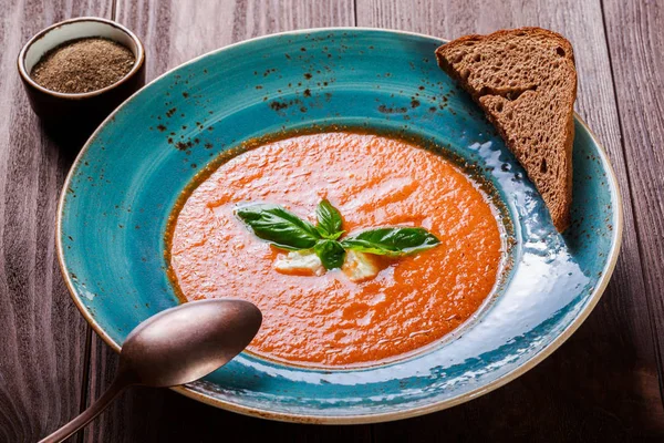 Sopa de gazpacho de tomate con albahaca, queso feta, hielo y pan sobre fondo de madera oscura, cocina española. Ingredientes en la mesa. Vista superior —  Fotos de Stock