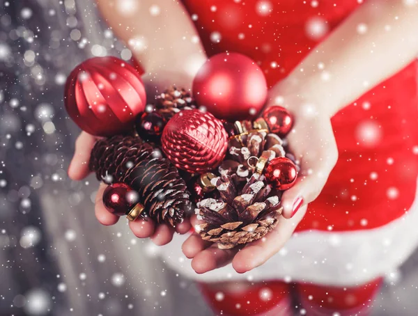 Mãos femininas segurando decorações de Natal vermelho e cones, fundo xmas brilhante. Presente de férias e ornamentos. Tonificação — Fotografia de Stock