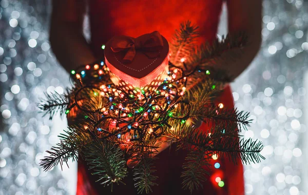 女性手里拿着圣诞礼物，分支的杉木树和多彩多姿光装饰，对黑暗假日背景. — 图库照片