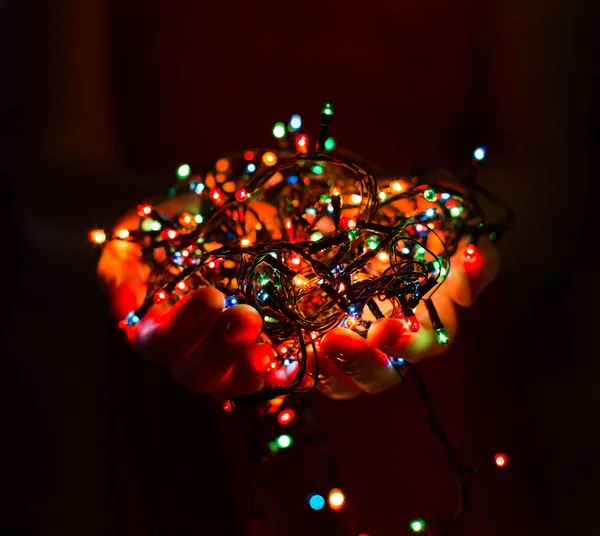 Çok renkli Noel ışık süslemeleri tatil koyu arka plan üzerinde tutan eller. Noel ve yeni yıl tema. Tonlama.