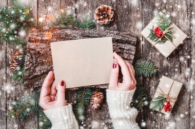 Noel hediyeleri, kabuk dokusu, çam dalları, çam kozalakları, kırmızı süslemeleri ile ahşap arka plan üzerinde Noel Baba'ya bir mektup yazma el. Noel ve mutlu yeni yıl kompozisyon. Düz yatıyordu, en iyi görünümü