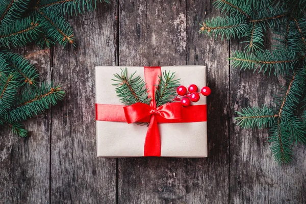 Confezione regalo di Natale con nastro rosso, rami di abete, fiocchi di neve su sfondo di legno. Natale e Felice Anno Nuovo composizione. Posa piatta, vista dall'alto — Foto Stock