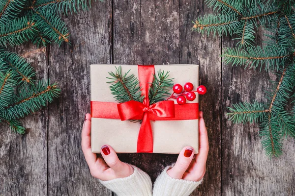 Female hands holding Christmas gift box with red ribbon on wooden background. Xmas and Happy New Year composition. Flat lay, top view — Stock Photo, Image