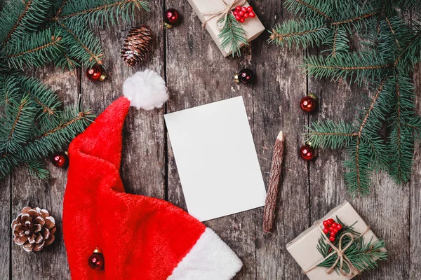 Kerst brief op houten achtergrond met rode kerstmuts, Fir takken, dennenappels, rode decoraties. Xmas en gelukkig Nieuwjaar samenstelling. Plat lag, top uitzicht — Stockfoto