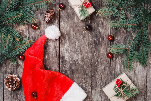 Composição de Natal com chapéu de Papai Noel vermelho, ramos de abeto, cones de pinheiro, decorações vermelhas em fundo de madeira. Cartão de Natal e Feliz Ano Novo. Deitado plano, vista superior — Fotografia de Stock