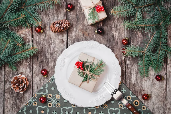 Assiette de Noël avec cadeau sur fond de vacances en bois avec, cônes de pin, décorations rouges, branches de sapin. Composition de Noël et Bonne Année. Couché plat, vue du dessus — Photo