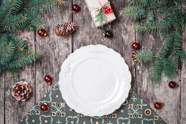 Рождественская тарелка на деревянном фоне праздника с подарком, сосновые шишки, красные украшения, еловые ветви. Композиция "С Новым годом и Рождеством". Плоский, вид сверху — стоковое фото