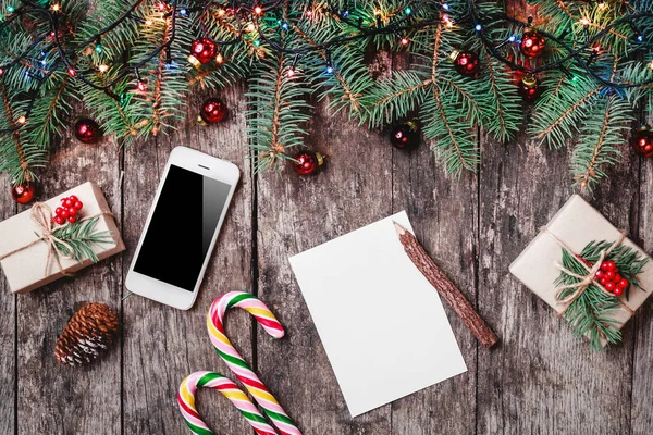 Cep telefonu, hediyeler, şeker, çam dalları, kırmızı süslemeleri ile ahşap arka plan üzerinde Noel mektubu. Noel ve mutlu yeni yıl kompozisyon. Düz yatıyordu, en iyi görünümü — Stok fotoğraf