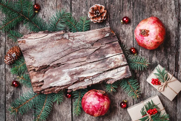 Vánoční složení s texturou kůry, vánoční dárky, granátové jablko, větve jedle na dřevěné pozadí. Vánoce a šťastný nový rok karty. Plochá ležel, horní pohled — Stock fotografie
