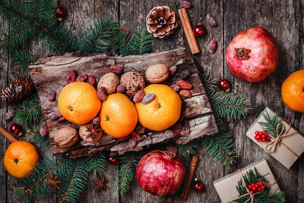 Vánoční přání. Vánoční dárky, granátová jablka, mandarinky, oříšky, kakaové boby, větve jedle na dřevěné zasněžené pozadí. Vánoce a šťastný nový rok složení. Pohled shora, Selektivní ostření — Stock fotografie