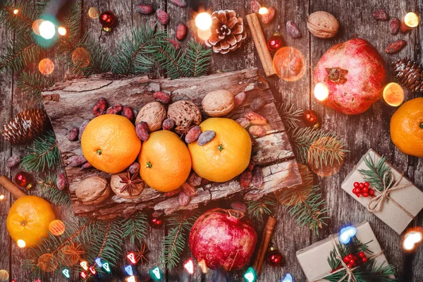 Vánoční přání. Vánoční dárky, granátová jablka, mandarinky, oříšky, kakaové boby, větve jedle na dřevěné zasněžené pozadí. Vánoce a šťastný nový rok složení. Pohled shora, Selektivní ostření — Stock fotografie