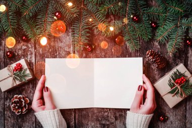 Noel hediyeleri, kabuk dokusu, çam dalları, çam kozalakları, kırmızı süslemeleri ile ahşap arka plan üzerinde Noel Baba'ya bir mektup yazma el. Noel ve mutlu yeni yıl kartı. Düz yatıyordu, en iyi görünümü
