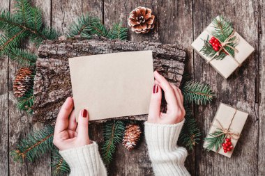 Noel hediyeleri, kabuk dokusu, çam dalları, çam kozalakları, kırmızı süslemeleri ile ahşap arka plan üzerinde Noel Baba'ya bir mektup yazma el. Noel ve mutlu yeni yıl kartı. Düz yatıyordu, en iyi görünümü