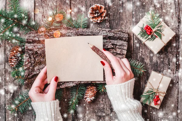 Noel hediyeleri, kabuk dokusu, çam dalları, çam kozalakları, kırmızı süslemeleri ile ahşap arka plan üzerinde Noel Baba'ya bir mektup yazma el. Noel ve mutlu yeni yıl kartı. Düz yatıyordu, en iyi görünümü