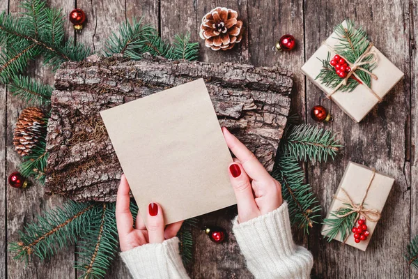Noel hediyeleri, kabuk dokusu, çam dalları, çam kozalakları, kırmızı süslemeleri ile ahşap arka plan üzerinde Noel Baba'ya bir mektup yazma el. Noel ve mutlu yeni yıl kartı. Düz yatıyordu, en iyi görünümü