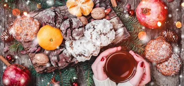 Žena rukou šálek čaje. Vánoční Cookies Čokoláda, čaj, granátové jablko, mandarinky, oříšky, kakaové boby na dřevěné zasněžené pozadí. Vánoce a šťastný nový rok karty. Pohled shora, Selektivní ostření — Stock fotografie