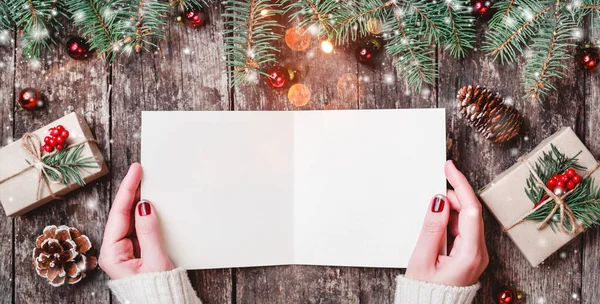 女性の手を書くと木製の背景にクリスマス プレゼント、モミの枝、お菓子をサンタさんへ手紙を読みます。クリスマスと新年のカード。フラット横たわっていた、トップ ビュー — ストック写真