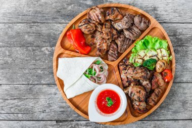 Çeşitli lezzetli ızgara et ve sebze taze salata ve kesme tahtası üzerinde ahşap arka plan barbekü sosu ile kapatın. Sıcak et yemekleri. Üstten Görünüm