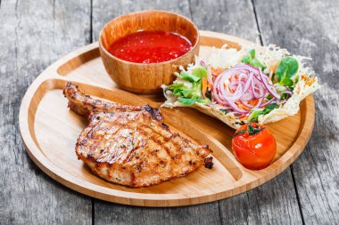 Izgara dana biftek kemik, taze salata, ızgara sebzeler ve kesme tahtası ahşap zemin üzerine domates sosu. Sıcak et yemekleri