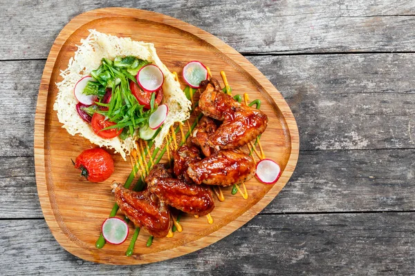Жареные куриные крылышки со свежим салатом, овощами на гриле и соусом барбекю на разделочной доске на деревянном фоне. Горячие мясные блюда. Вид сверху — стоковое фото