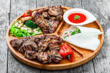 Çeşitli lezzetli ızgara et ve sebze taze salata ve kesme tahtası üzerinde ahşap arka plan barbekü sosu ile kapatın. Sıcak et yemekleri. Üstten Görünüm