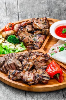 Çeşitli lezzetli ızgara et ve sebze taze salata ve kesme tahtası üzerinde ahşap arka plan barbekü sosu ile kapatın. Sıcak et yemekleri. Üstten Görünüm