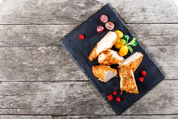 Gegrillte Hühnerbrüste mit Gemüse und Beeren auf Steinschieferhintergrund auf Holzhintergrund in Nahaufnahme. warme Fleischgerichte. Ansicht von oben — Stockfoto