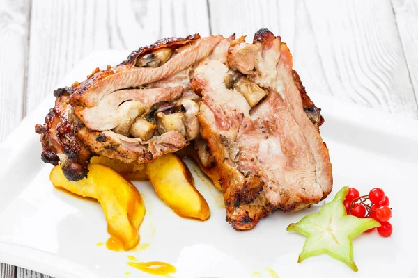 Schweinebraten gefüllt mit Pilzen, Pfirsich, Karambola, Preiselbeeren und süßer Sauce auf einem Teller auf hölzernem Hintergrund aus nächster Nähe. warme Fleischgerichte. Ansicht von oben — Stockfoto
