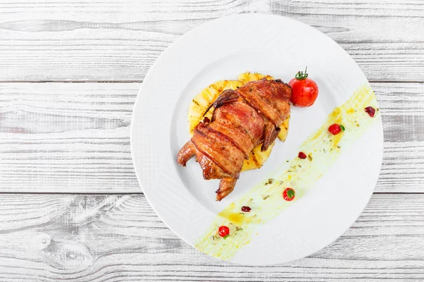 Жареная курица в ветчине с ананасом и помидорами на тарелке на деревянном фоне крупным планом. Горячие мясные блюда. Вид сверху . — стоковое фото