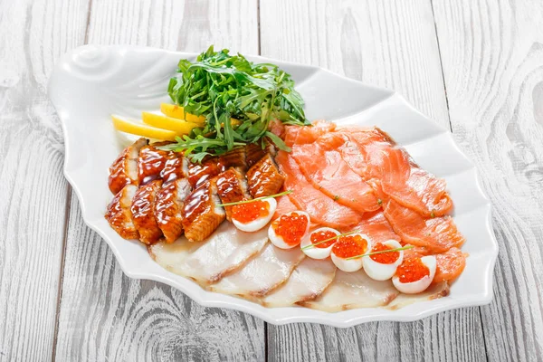 Seafood platter with salmon slice, smoke sturgeon, quail eggs with red caviar, slices fish fillet, decorated with arugula and lemon on wooden background close up. Mediterranean appetizers. Top view