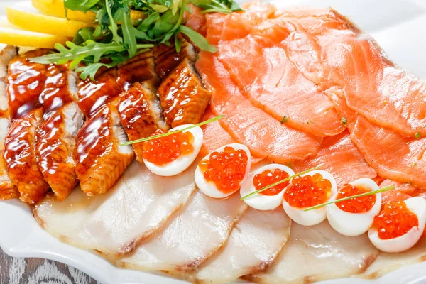 Seafood platter with salmon slice, smoke sturgeon, quail eggs with red caviar, slices fish fillet, decorated with arugula and lemon on wooden background close up. Mediterranean appetizers. Top view — Stock Photo, Image