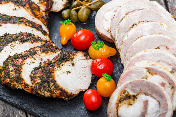 Slices of Homemade meatloaf, veal and pork tenderloin stuffed with vegetables on black slate stone chalkboard on wooden background close up. Meat appetizer. Top view