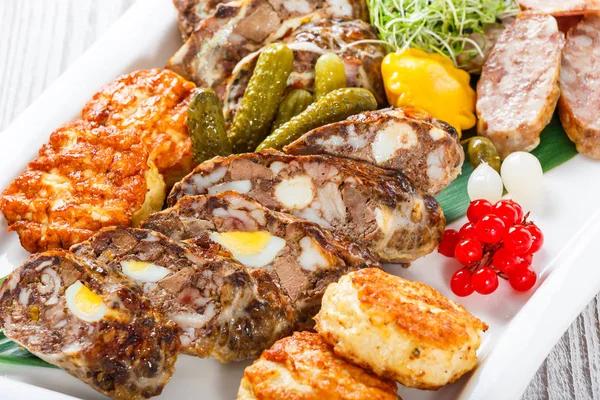 Saftige leckere Fleischschnitzel und hausgemachte Wurst mit eingelegtem Gemüse auf Teller auf Holzboden. Fleischvorspeise. Ansicht von oben — Stockfoto