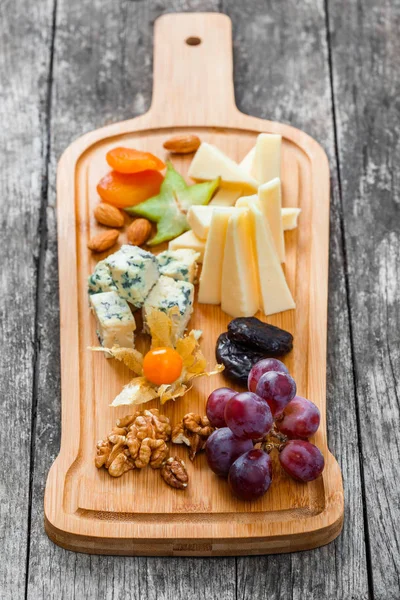 Plateau de fromage garni de poire, miel, noix, raisins, carambole, physalis sur planche à découper sur fond bois. Ensemble de collations et d'apéritifs au vin. Vue du dessus — Photo