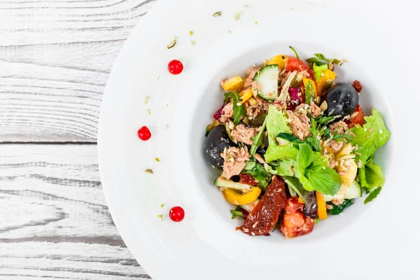 Frischer Salat mit Thunfisch, Rucola, Artischocken, Kabeljau, Oliven, Basilikum, sonnengetrockneten Tomaten, Kirschtomaten, Gurken, Blumenkohl auf Holzgrund aus nächster Nähe. Mittelmeerkost. Ansicht von oben — Stockfoto