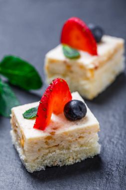 Mini kek çilek ve taş arduvaz arka plan üzerinde yaban mersini ile kapatın. Homemade pişirme. Düz yatıyordu, en iyi görünümü