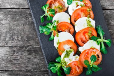 Mozzarella peyniri, domates, pesto sos ve fesleğen bitki Caprese salatası ahşap arka plan üzerinde siyah arduvaz taş kara tahta üzerinde yakın bırakır. Akdeniz sağlıklı gıda. Üstten Görünüm