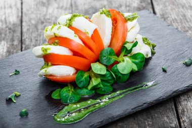 Mozzarella peyniri, domates, pesto sos ve fesleğen bitki Caprese salatası ahşap arka plan üzerinde siyah arduvaz taş kara tahta üzerinde yakın bırakır. Akdeniz sağlıklı gıda. Üstten Görünüm