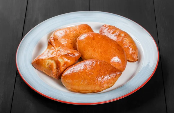 Färskt bröd bullar pajer färsbiffar i plattan på svart trä bakgrund. Bageriprodukter. Het och hälsosam frukost, ovanifrån, platt låg — Stockfoto