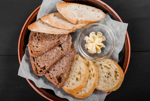 Pohled shora plátky celozrnné pečivo, ciabatta a žito klásky chleba s máslem na černém pozadí dřevěná. Pekařské výrobky. Svěží a zdravá snídaně, pohled shora, plochá ležel — Stock fotografie