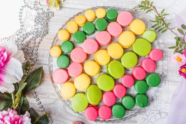 Macaroni saporiti variopinti su tavolo di legno con fiori, una delicatezza dolce francese, una struttura di macaron. Vista dall'alto, piatta — Foto Stock