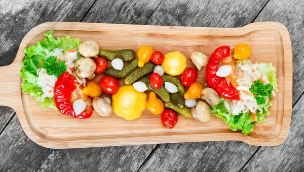 Surtido de verduras en escabeche: repollo chucrut, pimientos, pepinos, tomates, cebollas, champiñones y hierbas en la tabla de cortar sobre fondo de madera de cerca. Snacks y aperitivos de vino establecidos. Vista superior — Foto de Stock