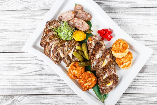 Saftige leckere Fleischschnitzel und hausgemachte Wurst mit eingelegtem Gemüse auf Teller auf Holzboden. Fleischvorspeise. Ansicht von oben — Stockfoto