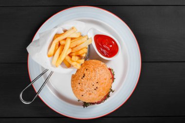 Hamburger, patates kızartması, ketçap, mayonez, taze sebze ve koyu ahşap arka plan üzerinde plaka üzerinde peynir ile hamburger. Amerikan fast food. Üstten Görünüm